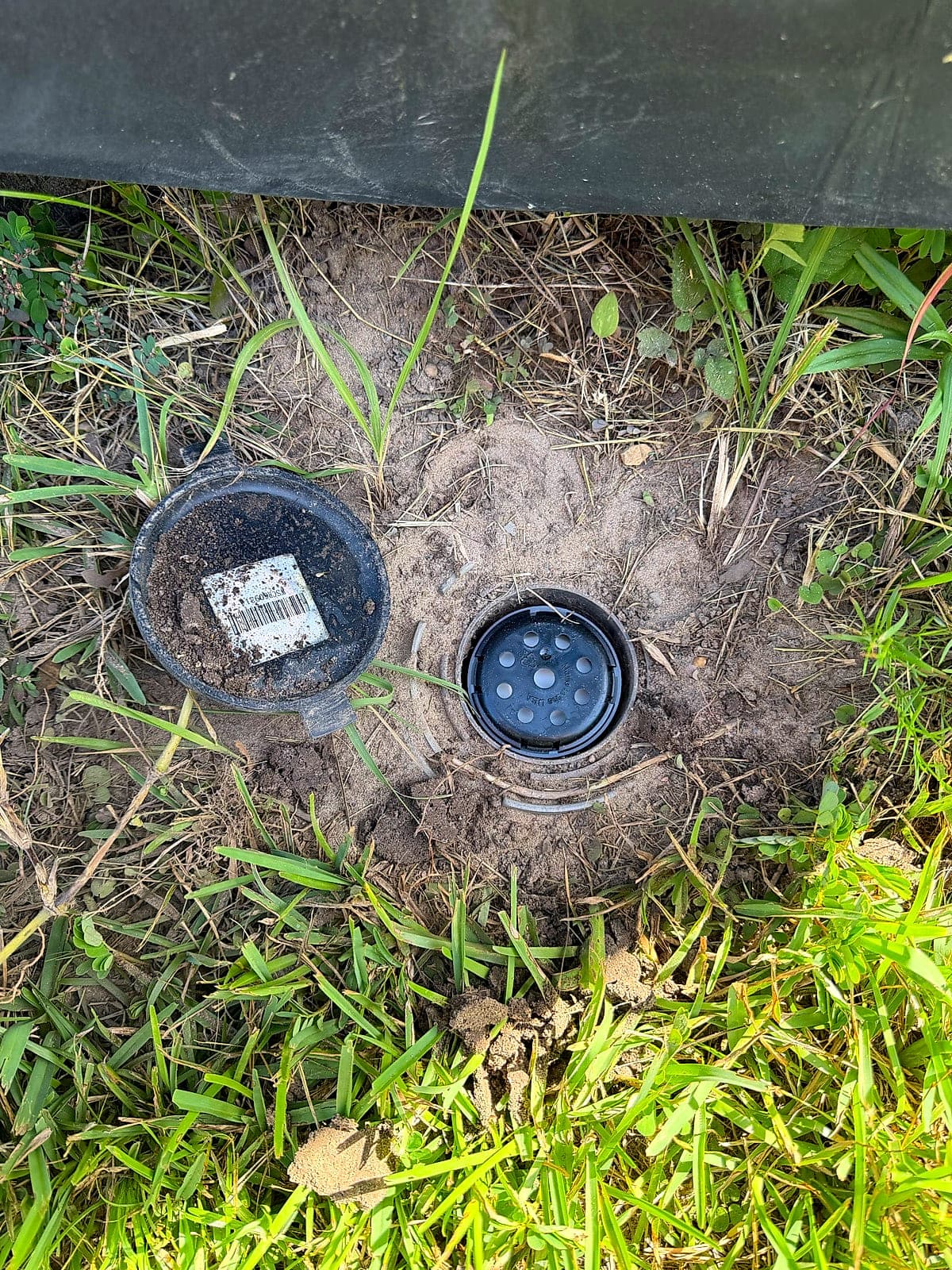 An in-ground termite bait station set into the soil beside a structure, cap off