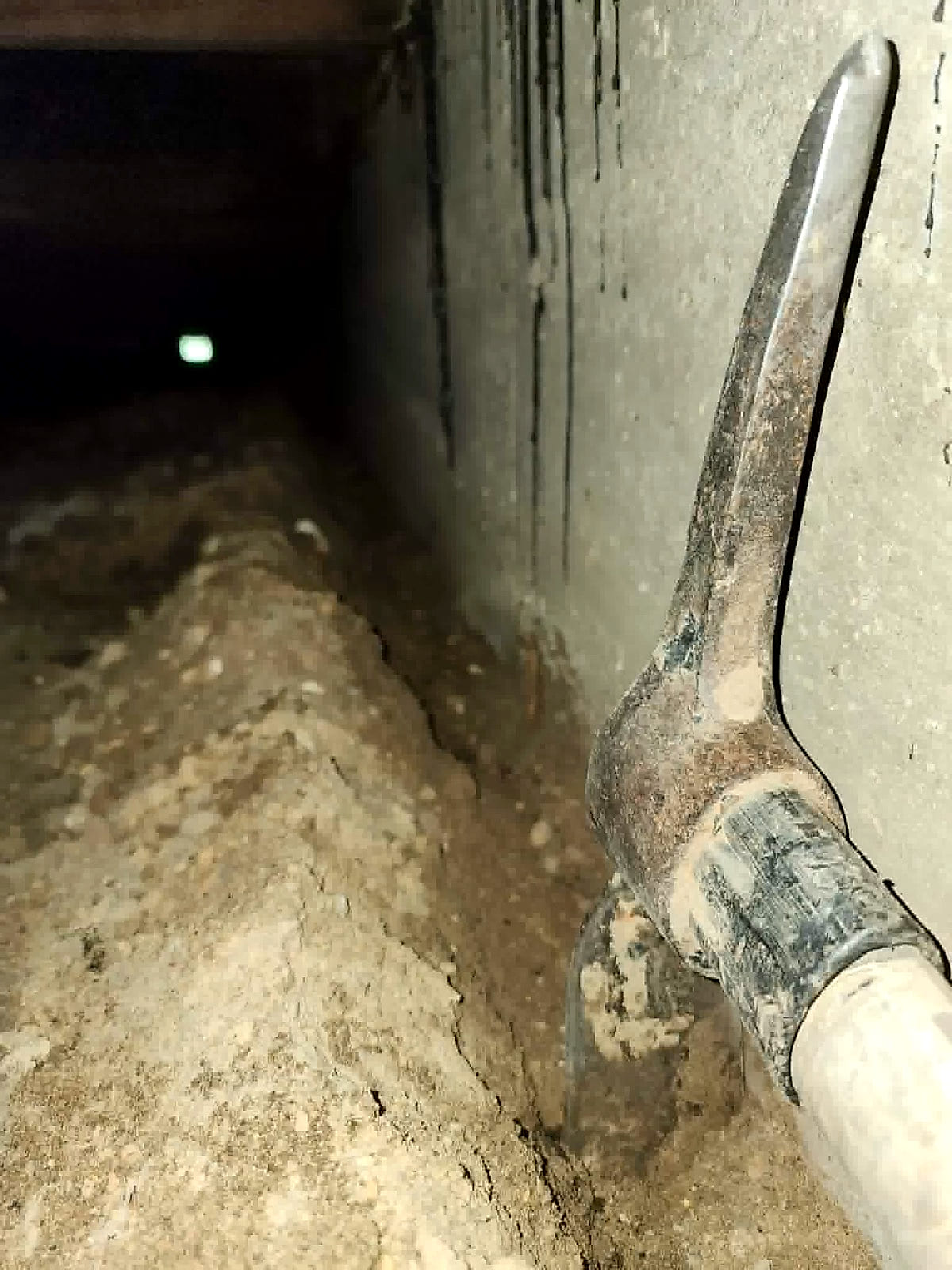 A trench being cut along a foundation wall with a mattock